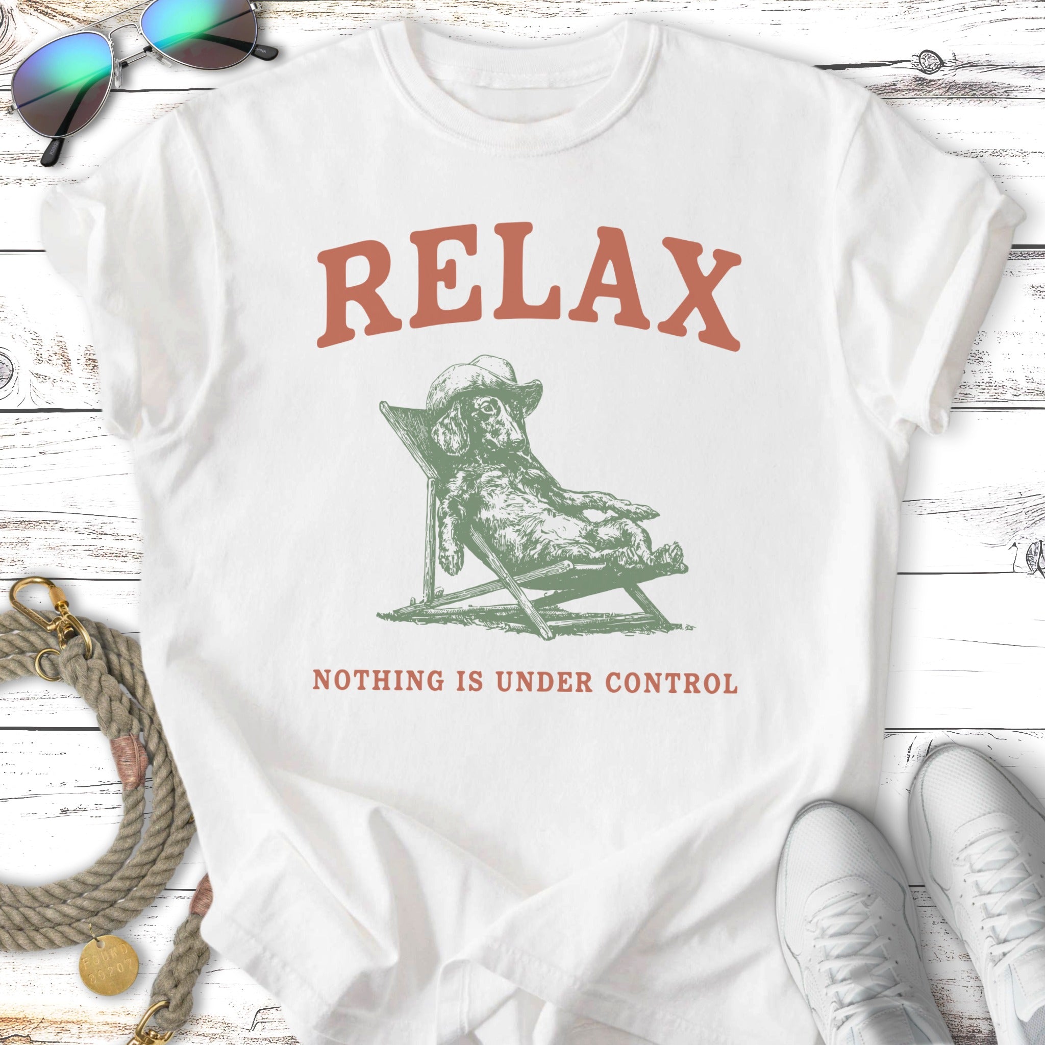 White t-shirt with green graphic of dog relaxing in chair, "RELAX NOTHING IS UNDER CONTROL".