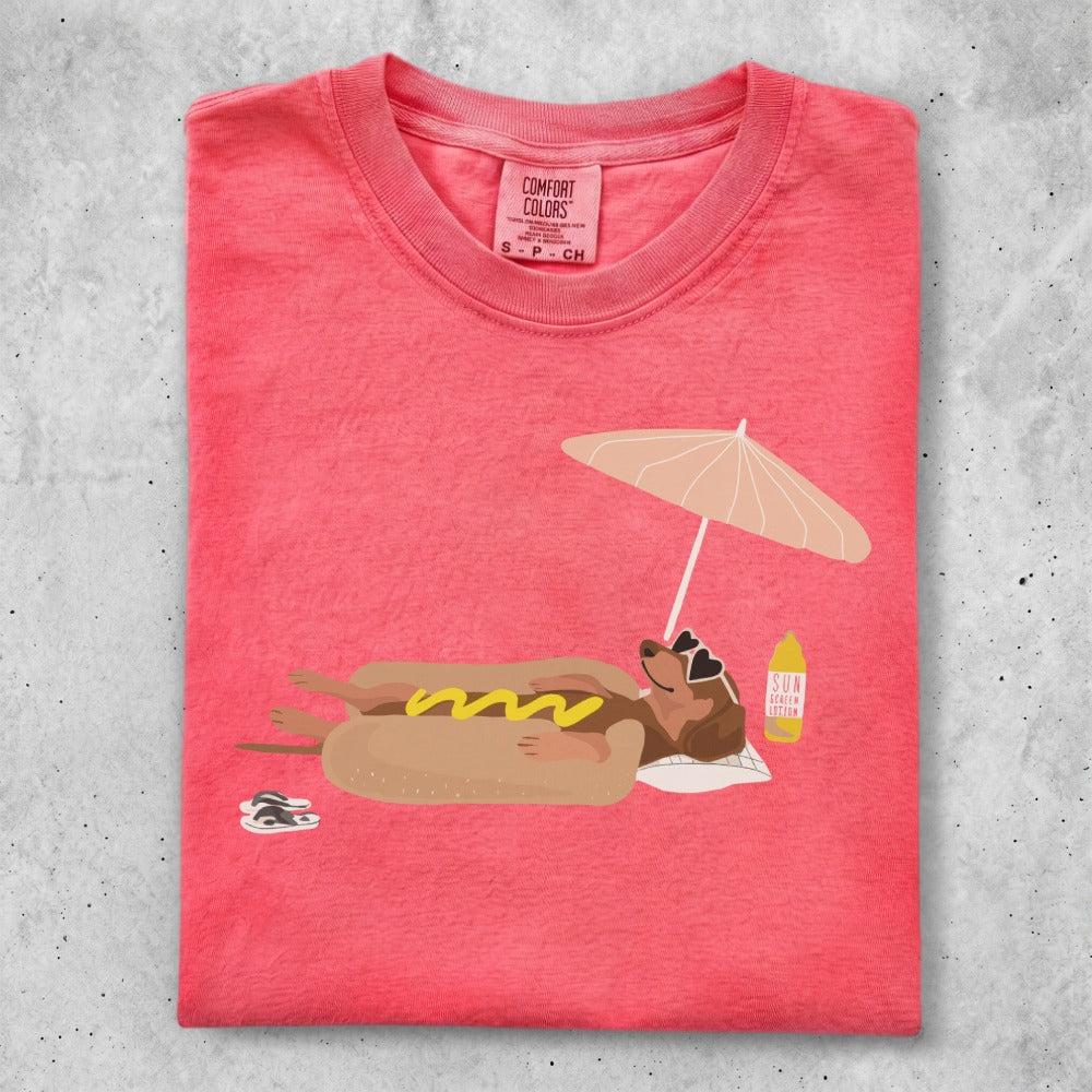 T-shirt with dachshund in hot dog costume lounging under umbrella with sunscreen.