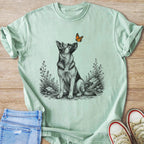 German Shepherd sitting in wildflowers, looking up at a butterfly.