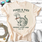 Cream t-shirt with cat wearing chef hat, "Purrs & Pies Pizza Co. Whisker Licken' Good".
