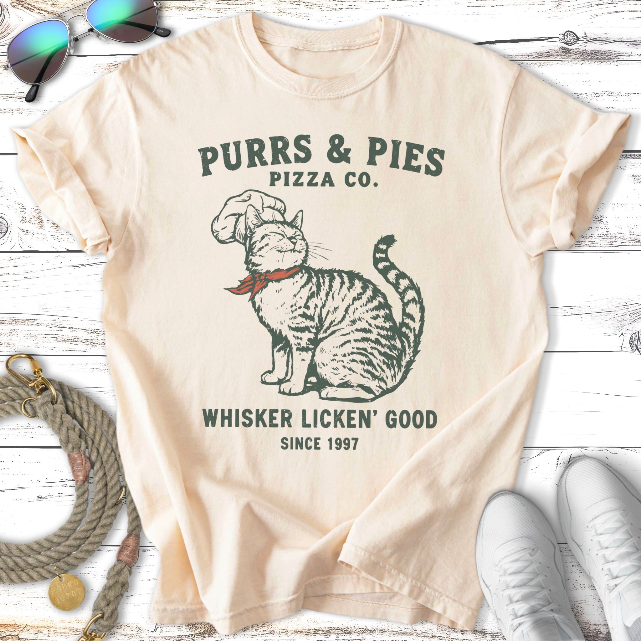 Cream t-shirt with cat wearing chef hat, "Purrs & Pies Pizza Co. Whisker Licken' Good".