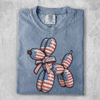 Blue t-shirt with a balloon dog design featuring American flag patterns and a red and white striped bow.