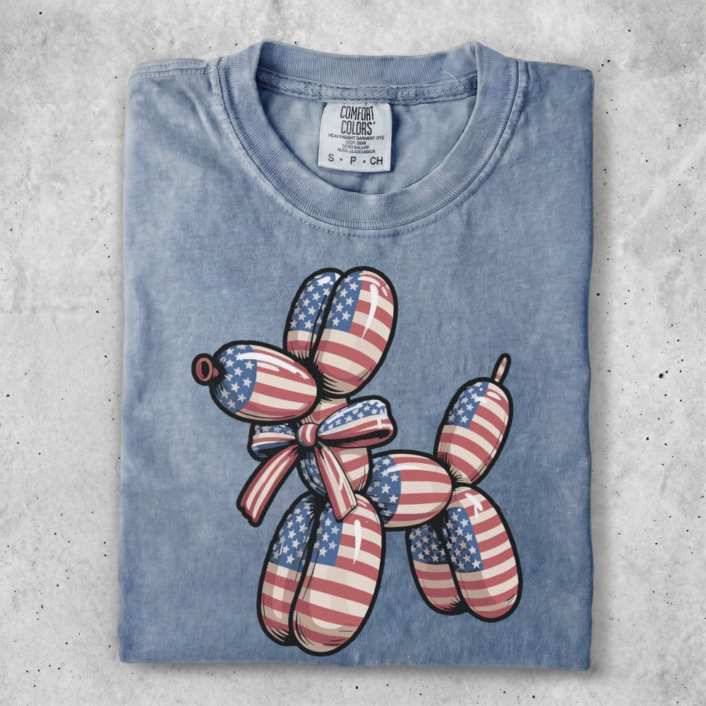 Blue t-shirt with a balloon dog design featuring American flag patterns and a red and white striped bow.