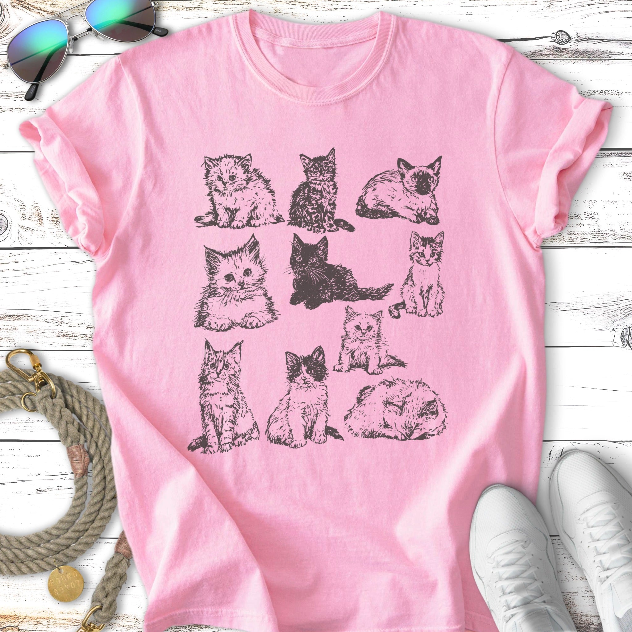 Nine different kittens sketched on a pink t-shirt.