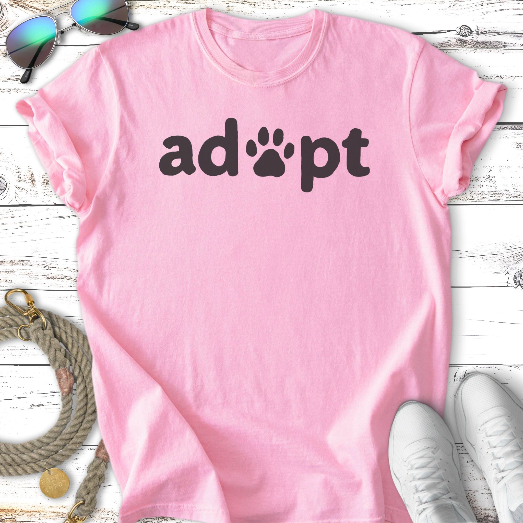 Pink t-shirt with "adopt" and a paw print in black text.