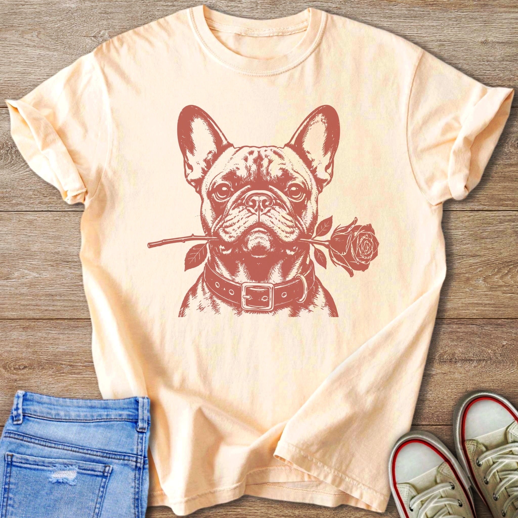 French bulldog with a rose in its mouth printed on a light peach t-shirt.