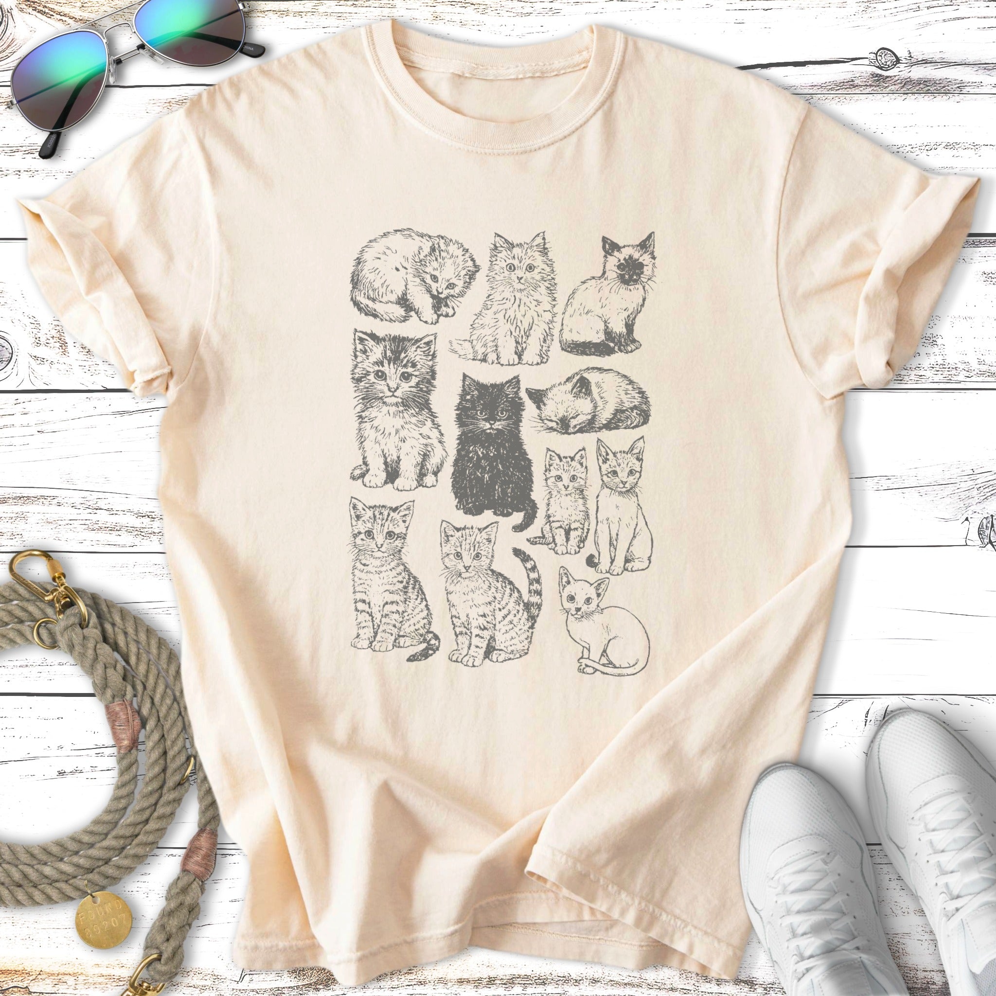 Line drawing of twelve different cats in a grid on a cream t-shirt.