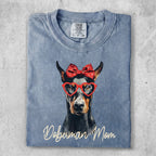 Doberman dog wearing red heart glasses and a red bow, with "Doberman Mom" text.