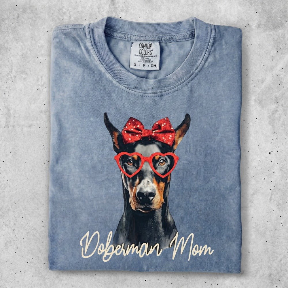 Doberman dog wearing red heart glasses and a red bow, with "Doberman Mom" text.