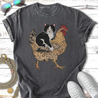 Black and white cat riding a chicken on a dark grey t-shirt.