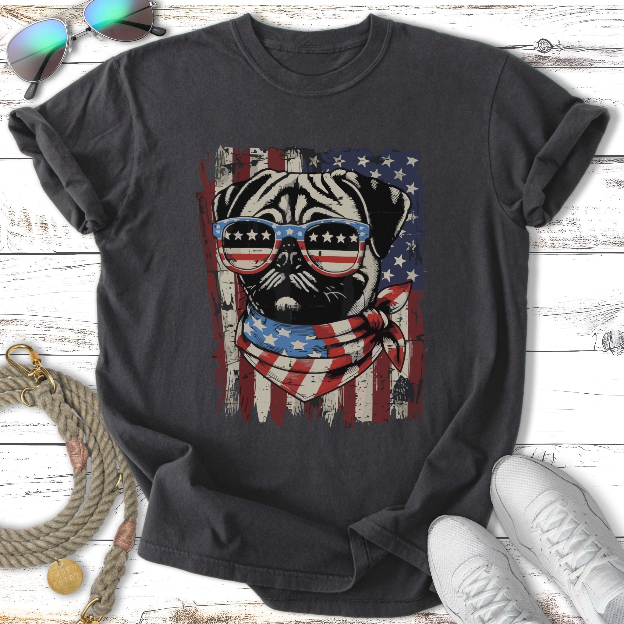 Pug wearing sunglasses and bandana against American flag design on dark t-shirt.