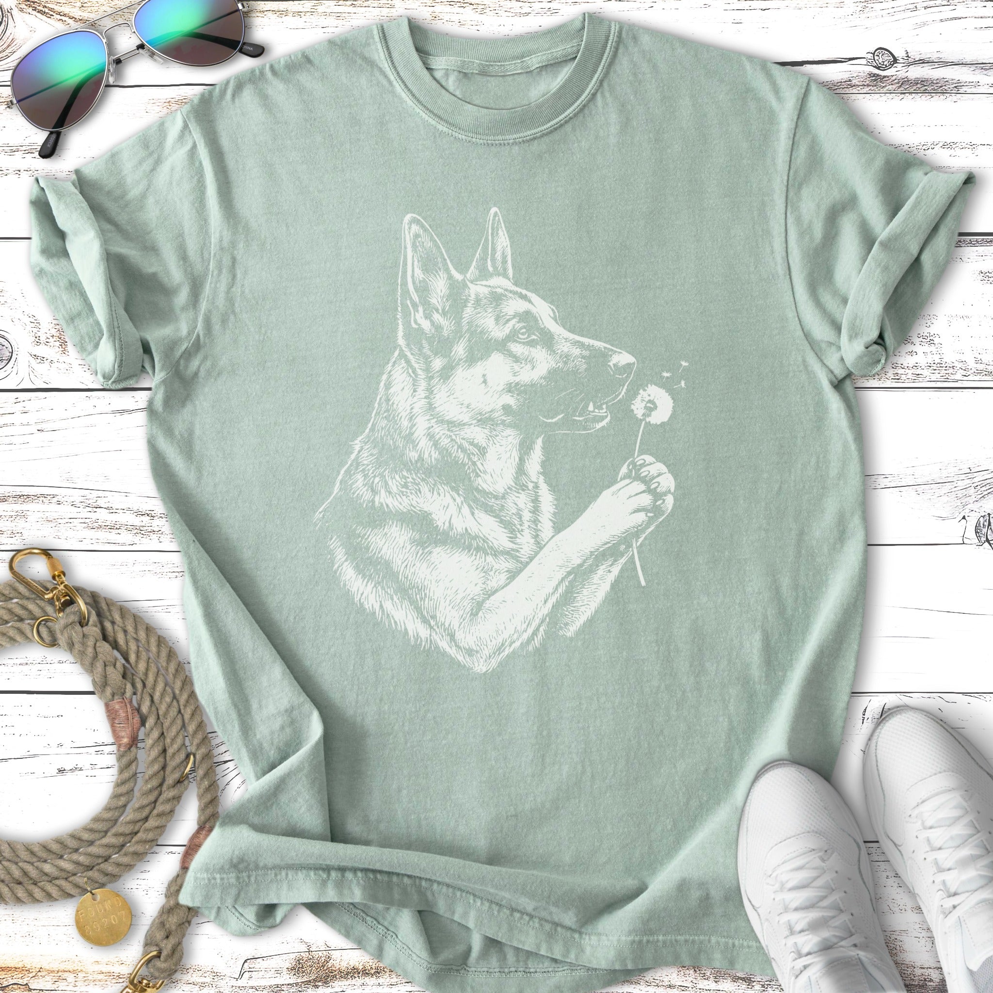 Line drawing of a German Shepherd holding a dandelion against a light green t-shirt.