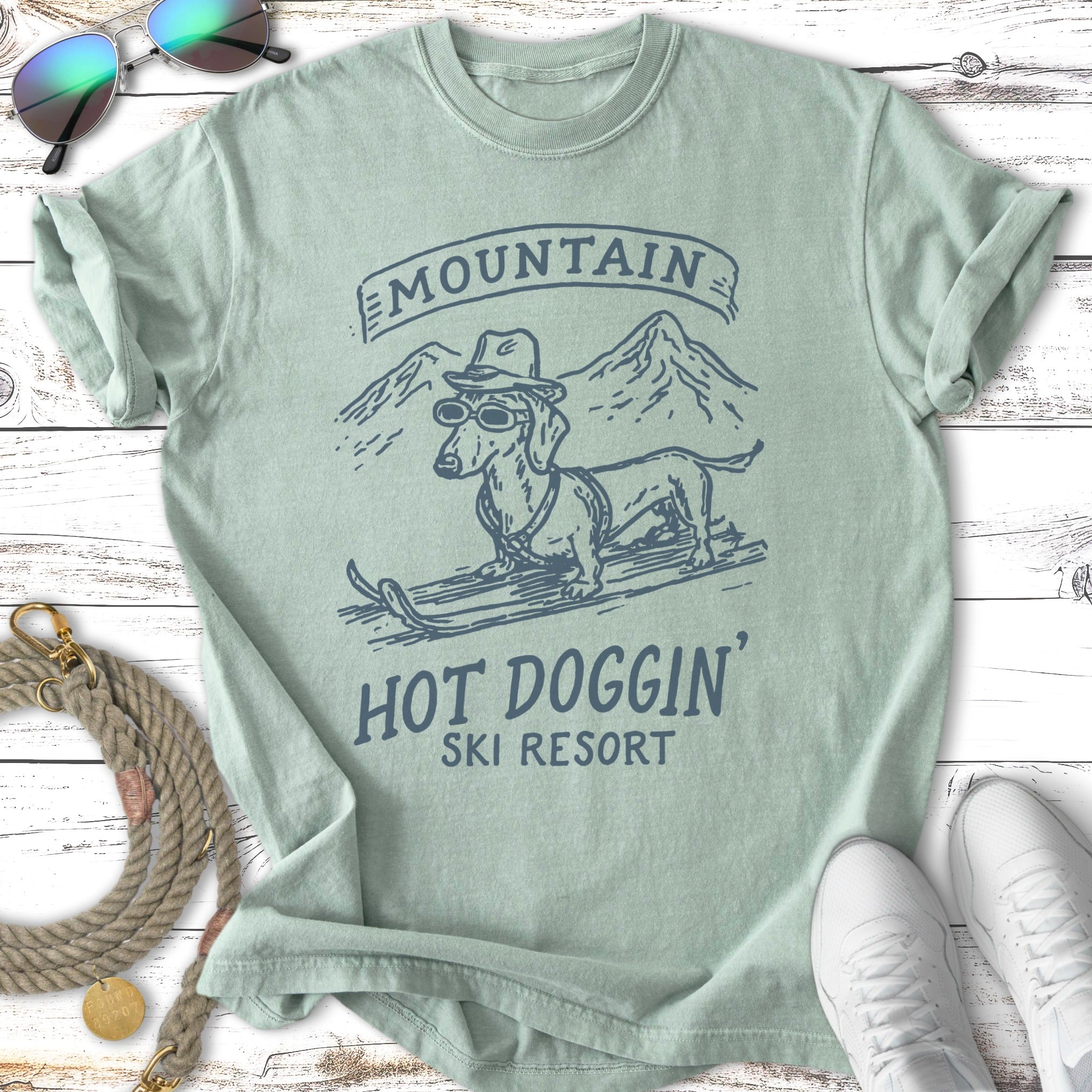 Dachshund wearing sunglasses and hat on skis, "Mountain Hot Doggin' Ski Resort" text.