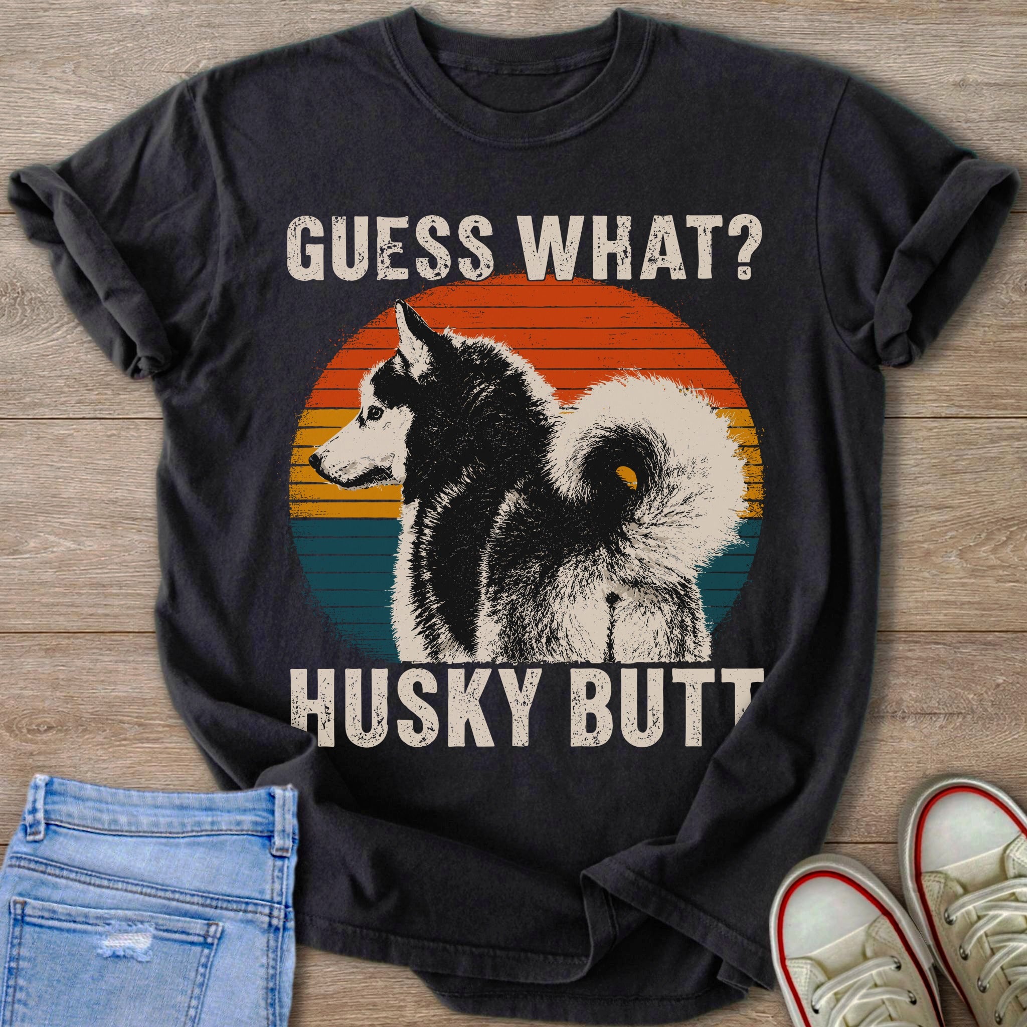 Black t-shirt on wooden background with husky graphic and text "GUESS WHAT? HUSKY BUTT".
