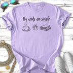 Lavender t-shirt with "My needs are simple" and icons of coffee, books, and a paw print.