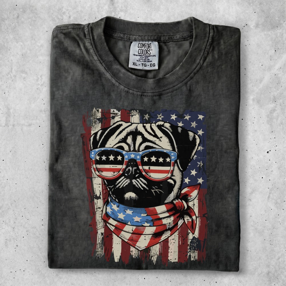 Pug wearing patriotic sunglasses and bandana against American flag background.