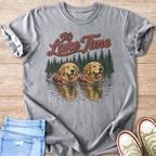 Two golden retrievers in life vests swim in a lake with pine trees.