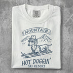 White t-shirt with graphic of a dachshund in sunglasses skiing, "Mountain Hot Doggin' Ski Resort" text.