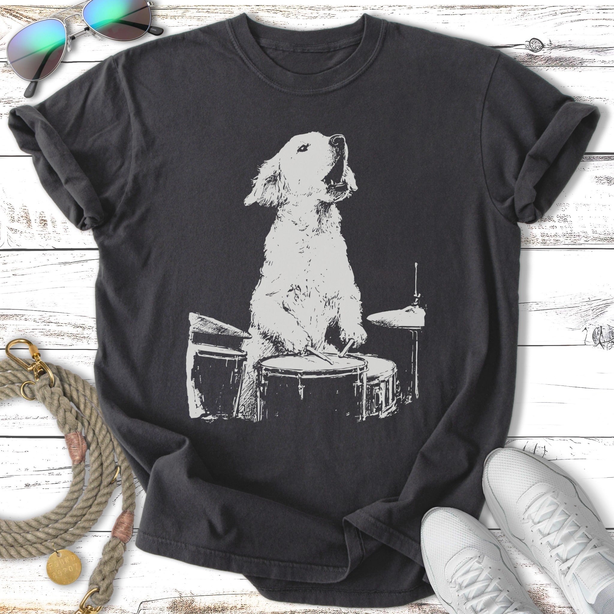 White sketch of a golden retriever playing a drum set on a dark t-shirt.