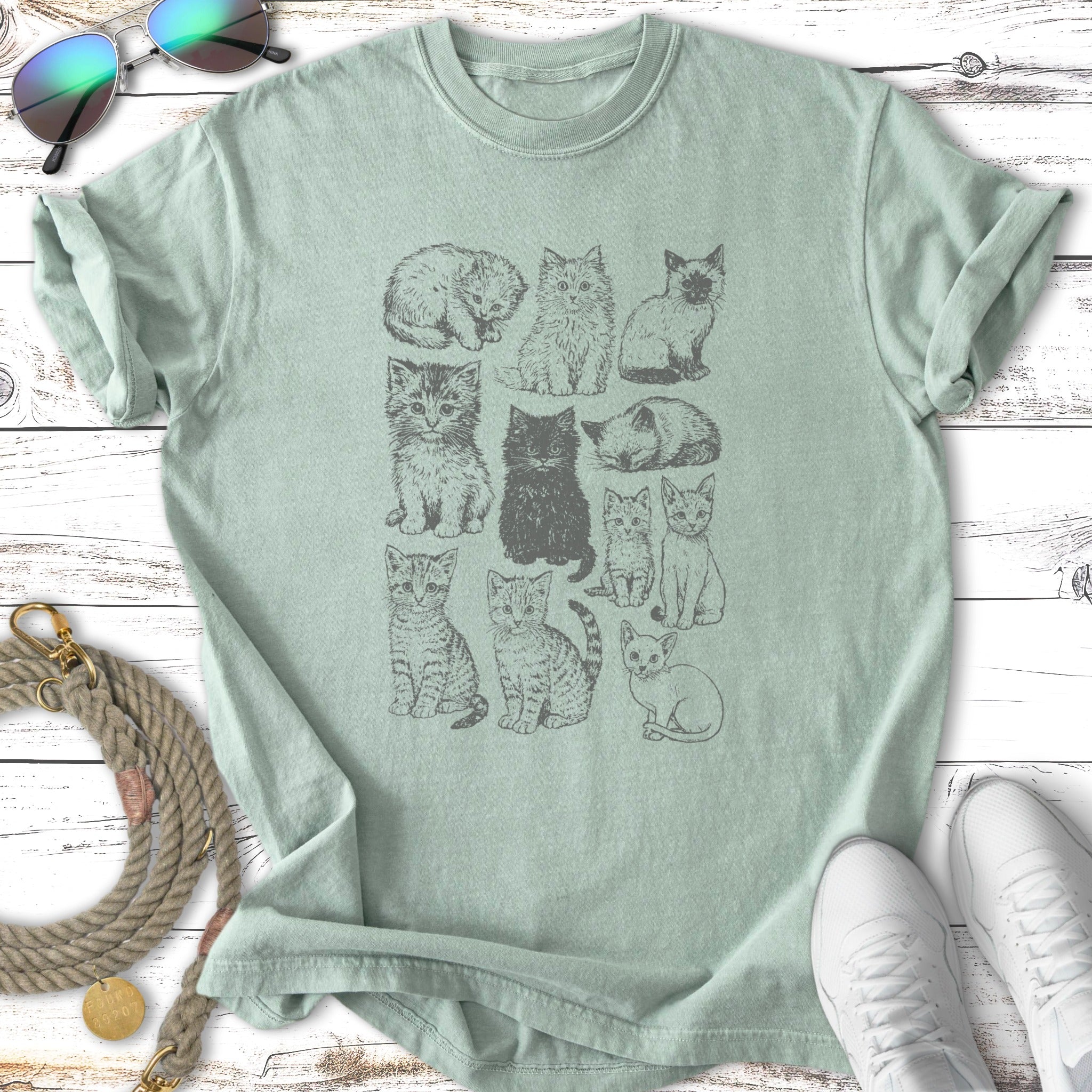 Grid of twelve small illustrated cats in different poses on a light green t-shirt.
