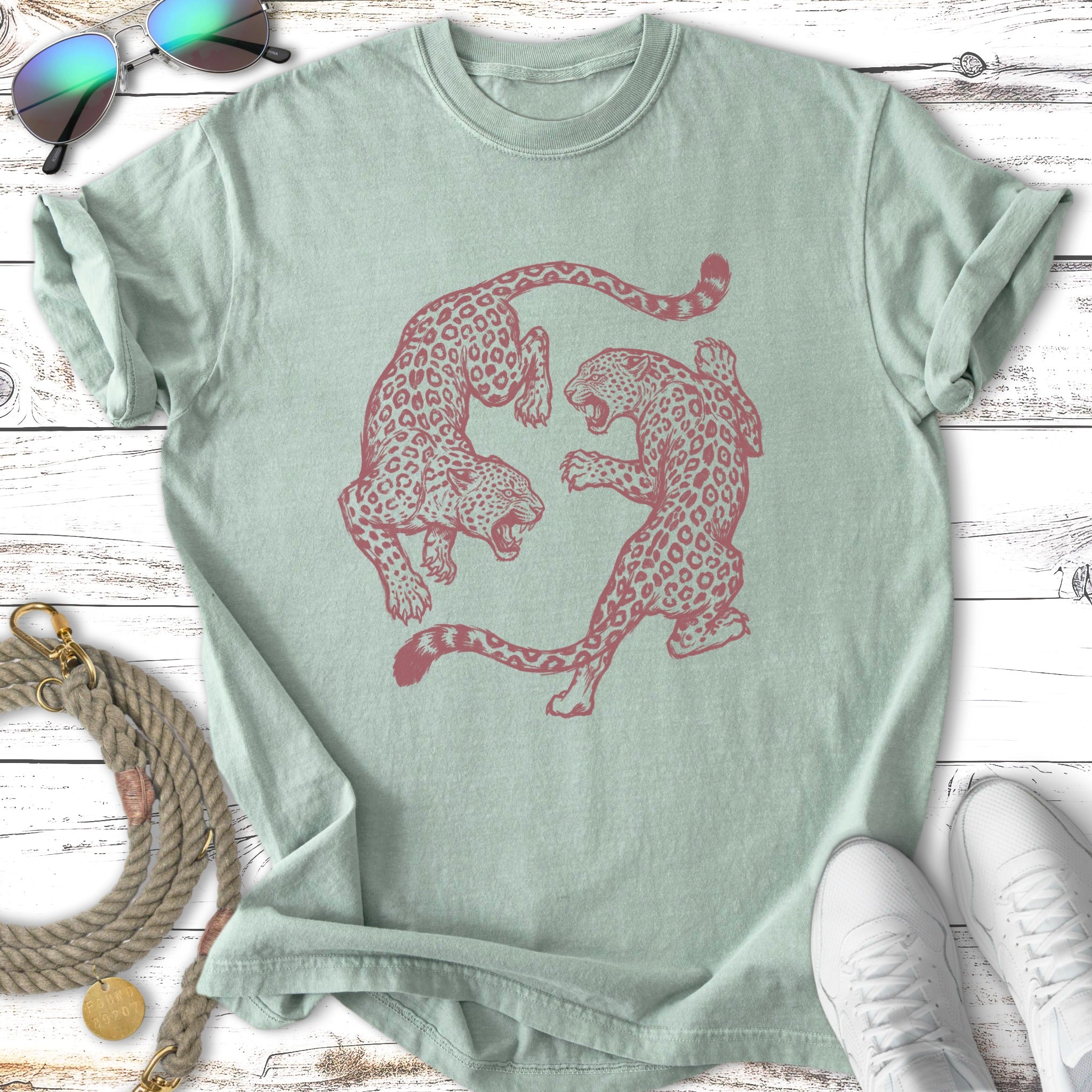 Two stylized leopards in a circular, decorative pattern on a pale green t-shirt.