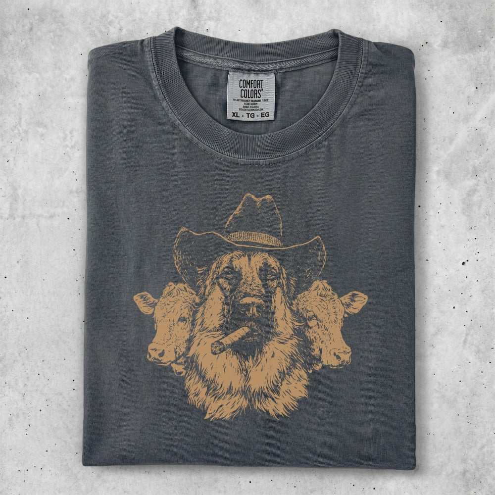 German Shepherd in cowboy hat with cows, wearing a graphic t-shirt.