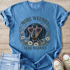 Blue t-shirt with dachshund wearing heart glasses, surrounded by flowers, saying "More Weenies Less Meanies".