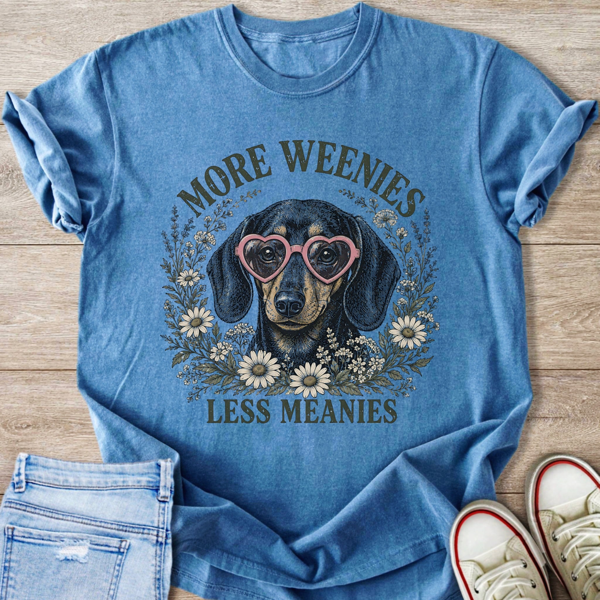 Blue t-shirt with dachshund wearing heart glasses, surrounded by flowers, saying "More Weenies Less Meanies".