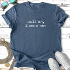 Blue t-shirt with "hold on, I see a cat" text, sunglasses, leash, and sneakers.