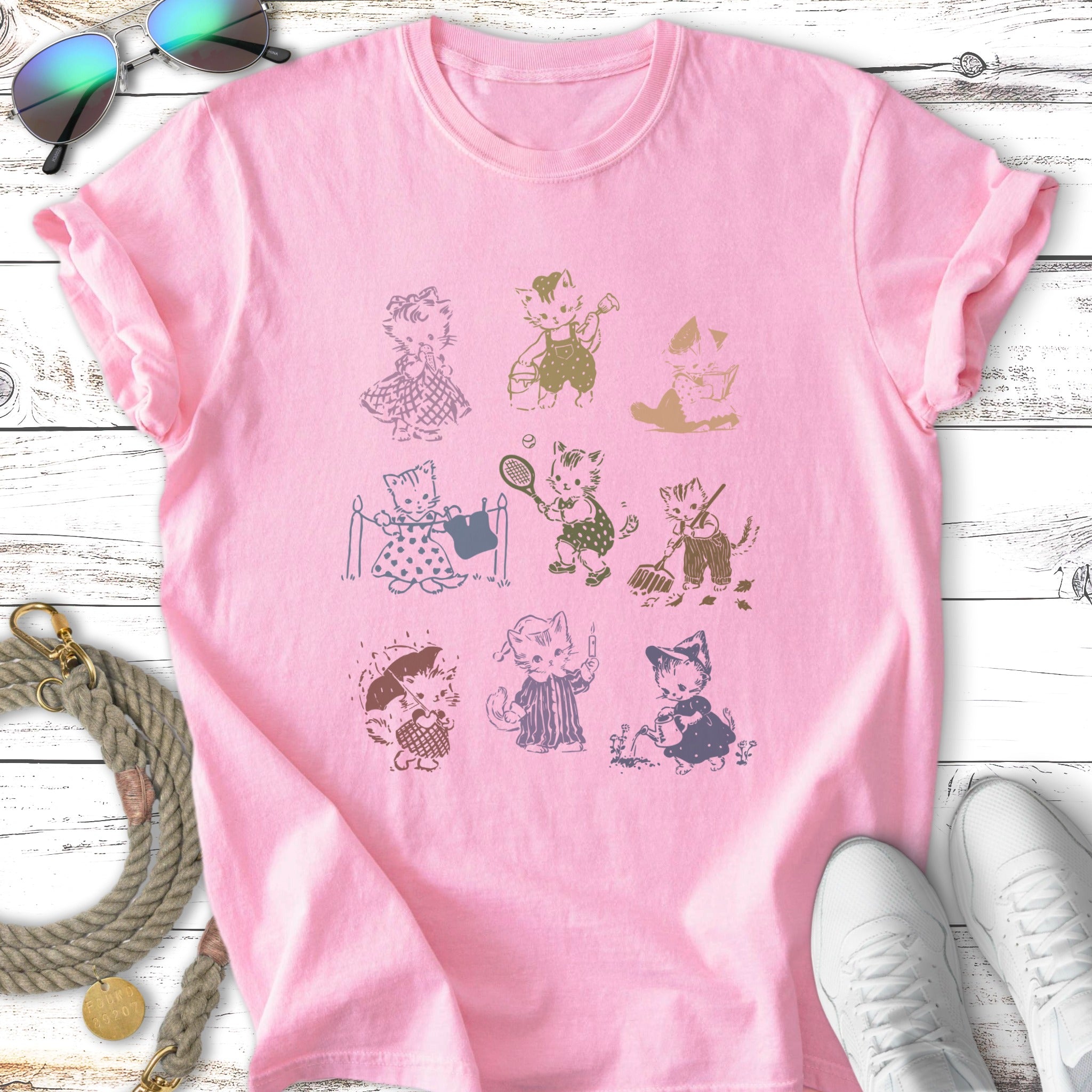 Pink t-shirt featuring a grid of nine cartoon cats in various activities.
