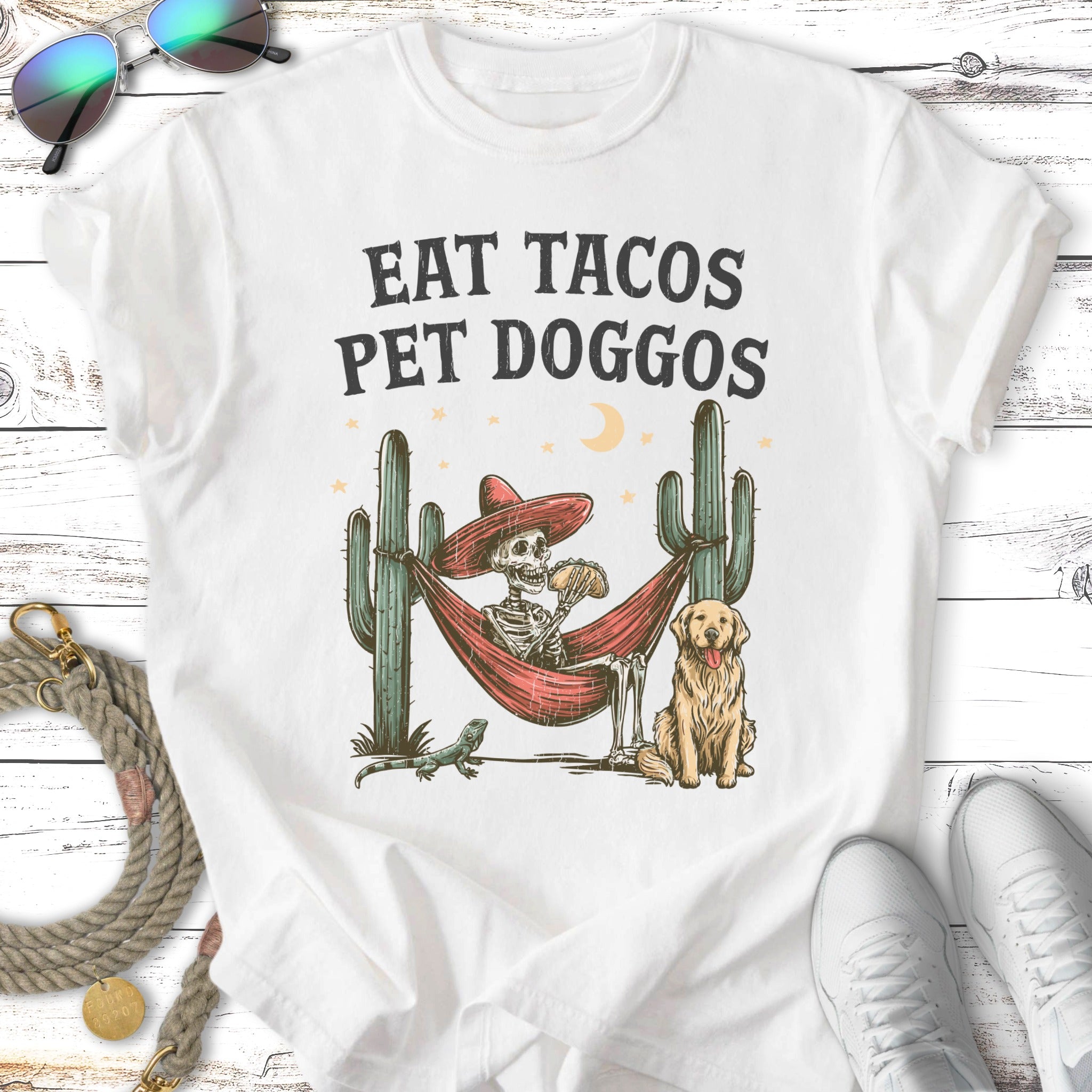 Skeleton in hammock eating tacos, dog, cacti, and lizard.