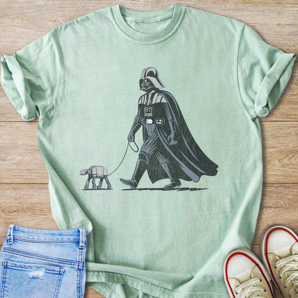 Darth Vader walks an AT-ST walker on a leash on a light green t-shirt.