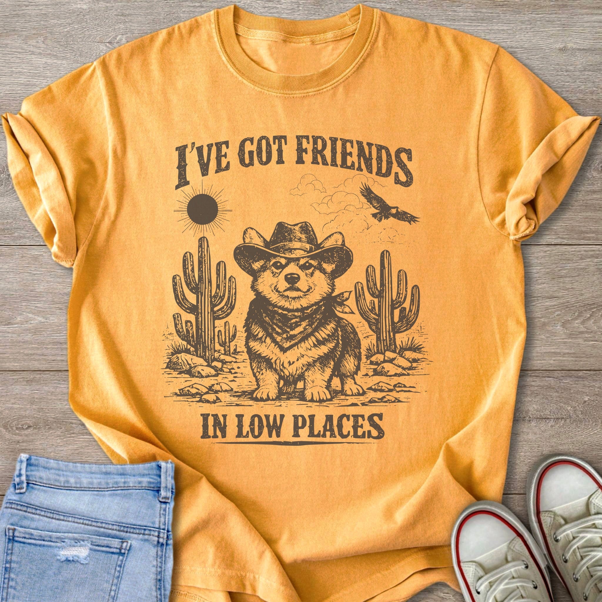 Yellow t-shirt with cowboy corgi, cacti, sun, eagle, and text "I'VE GOT FRIENDS IN LOW PLACES".