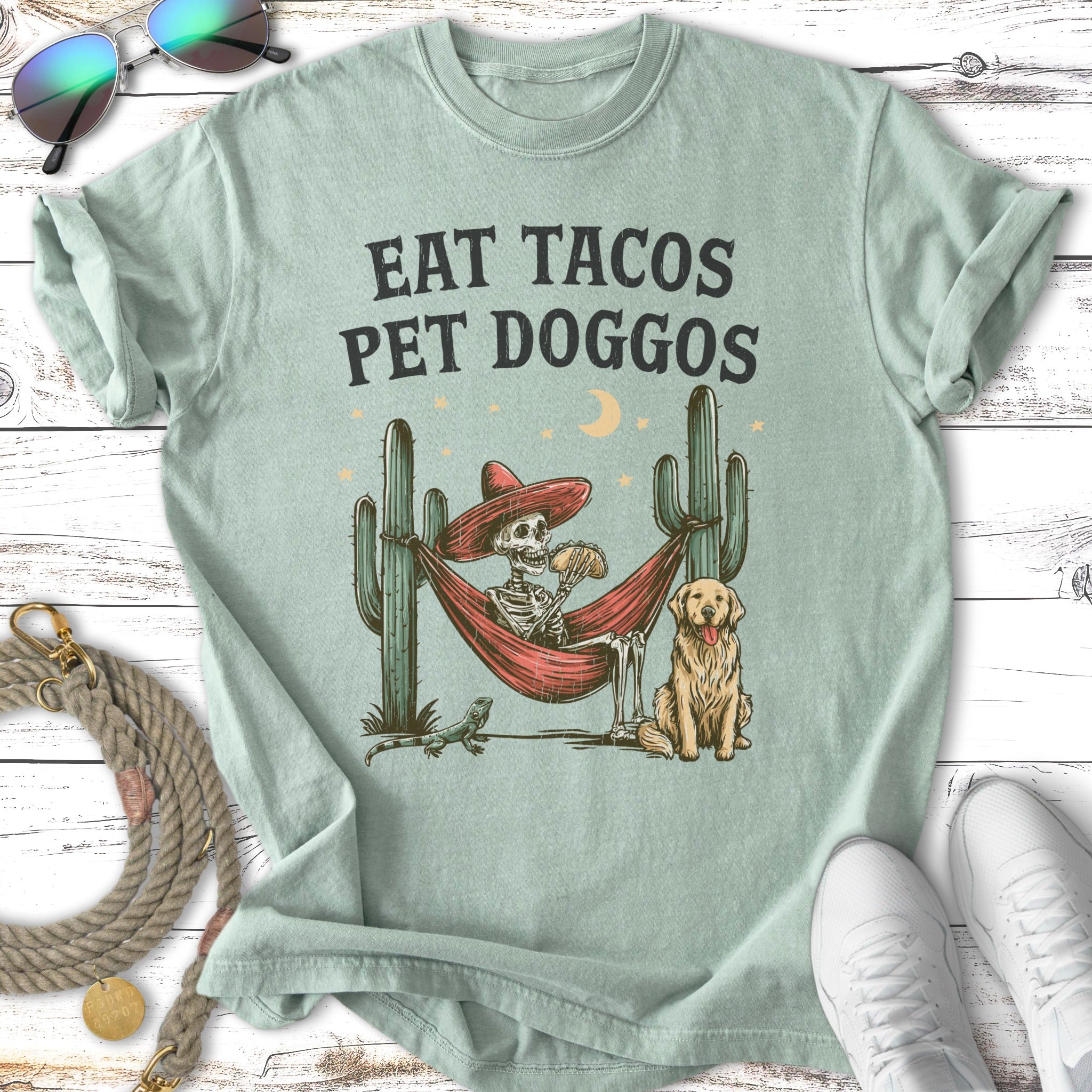 Skeleton in hammock eating tacos with dog and cactus.