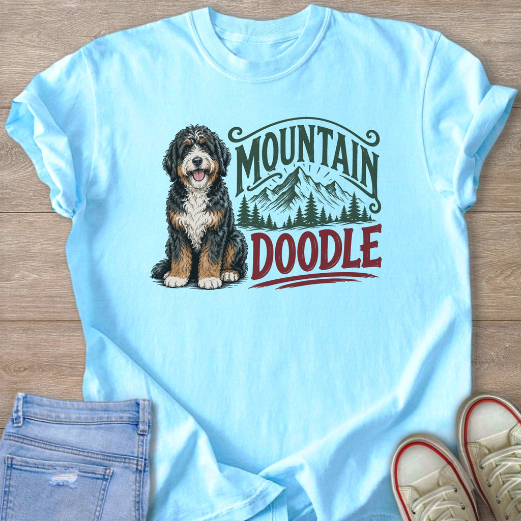 Bernedoodle dog with "Mountain Doodle" text and mountain graphics on light blue t-shirt.
