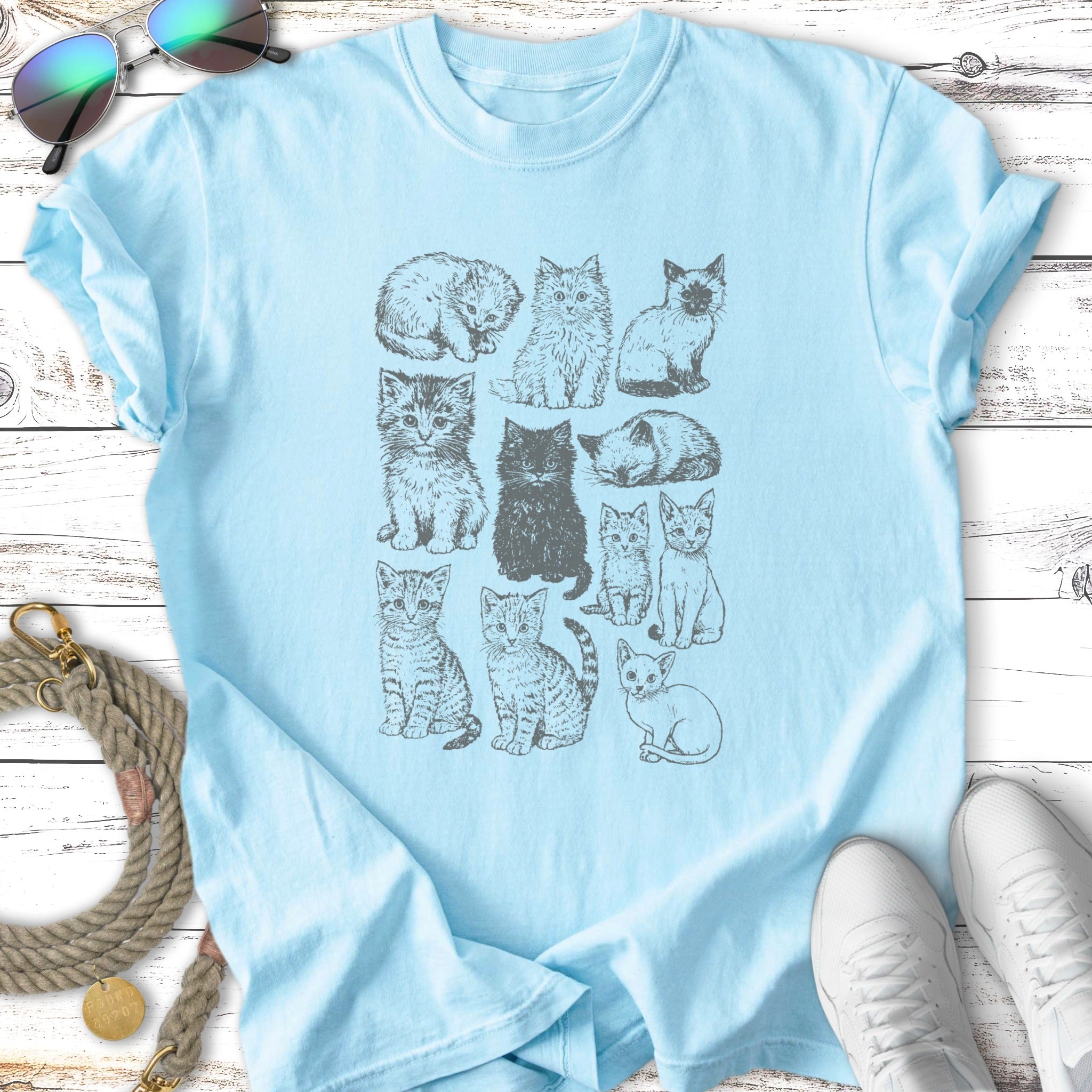 Light blue t-shirt with a grid of twelve different cat illustrations.