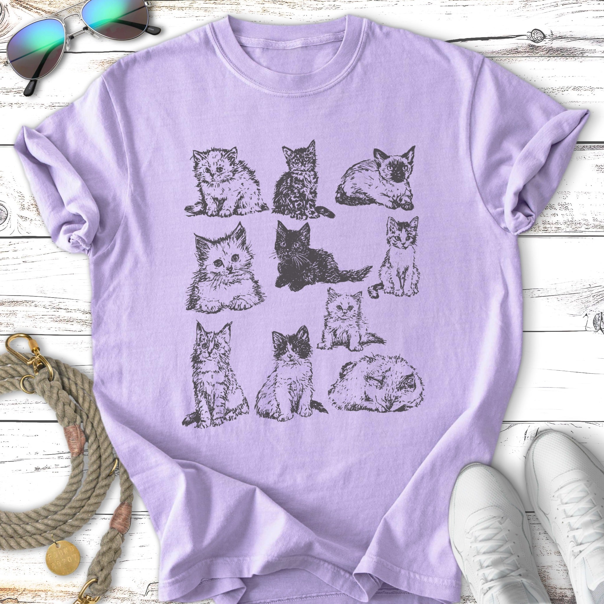 Nine different illustrated cats in a grid pattern on a lavender t-shirt.