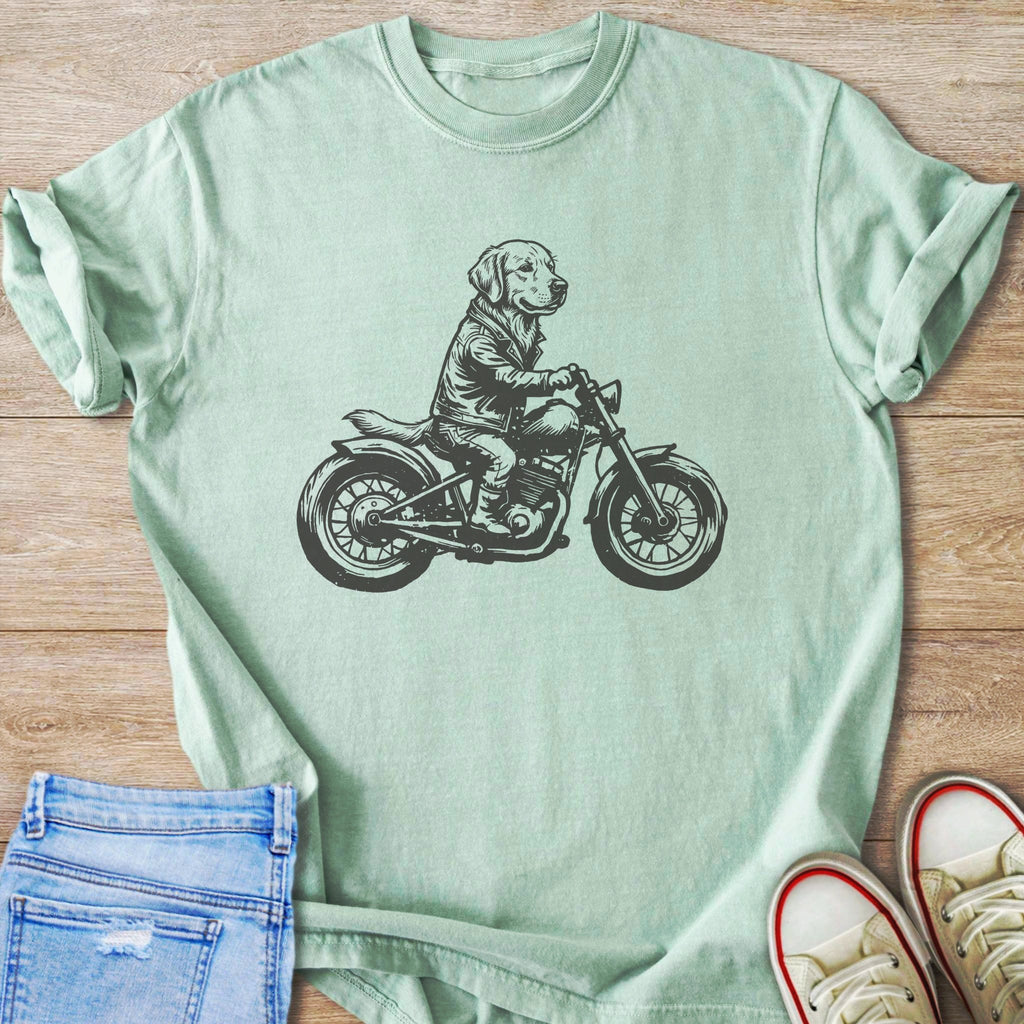 Line art of a dog wearing a jacket riding a motorcycle on a mint green t-shirt.
