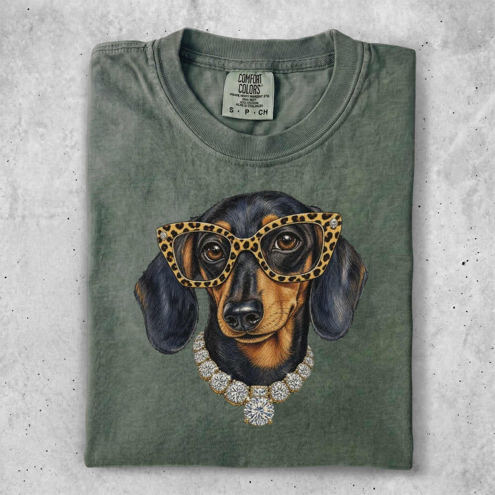 Dachshund wearing glasses and diamond necklace on olive green t-shirt.