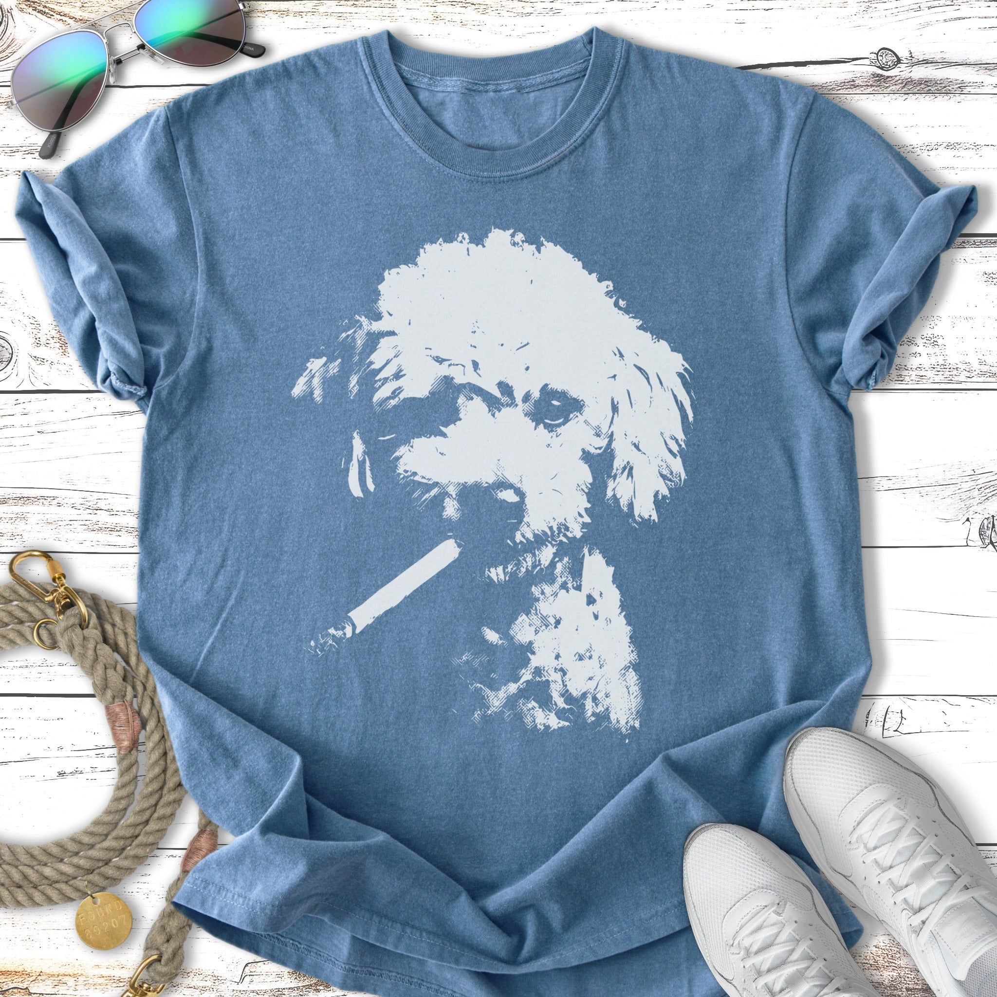 T-shirt with white poodle smoking a cigarette, laid flat with sneakers and sunglasses.