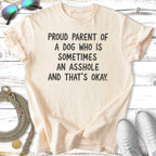 Cream t-shirt with text "PROUD PARENT OF A DOG WHO IS SOMETIMES AN ASSHOLE AND THAT'S OKAY."