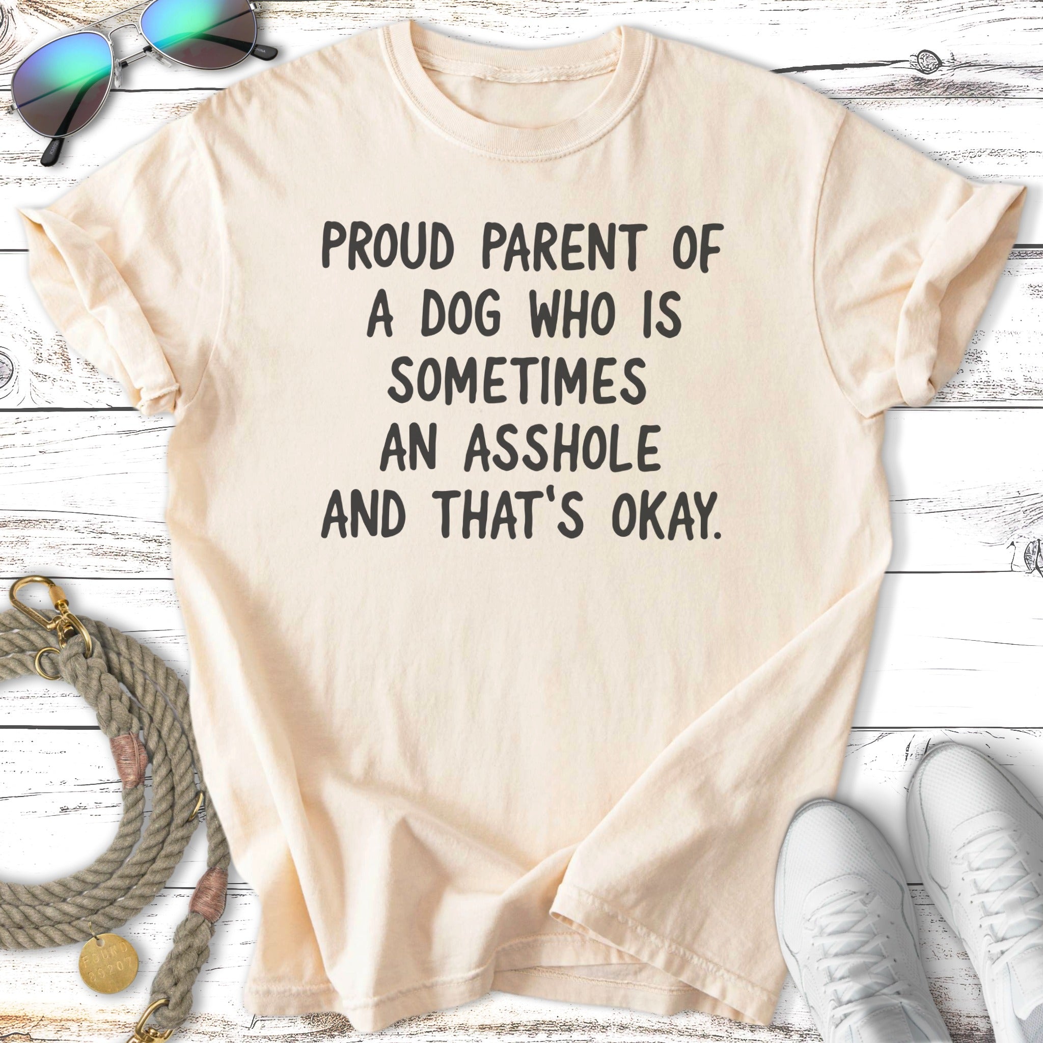 Cream t-shirt with text "PROUD PARENT OF A DOG WHO IS SOMETIMES AN ASSHOLE AND THAT'S OKAY."
