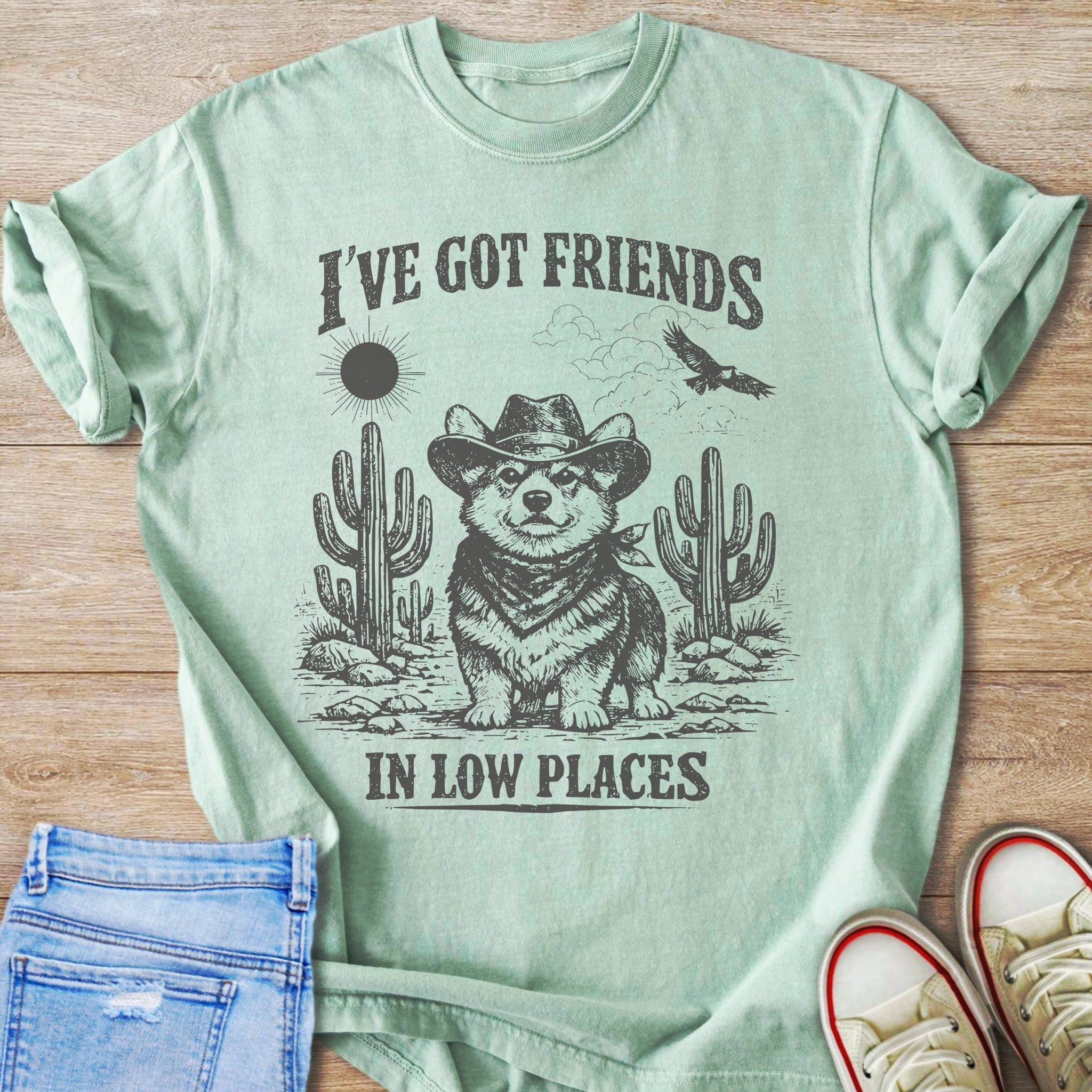 Light green t-shirt with a graphic of a corgi wearing a cowboy hat and bandana in a desert landscape.