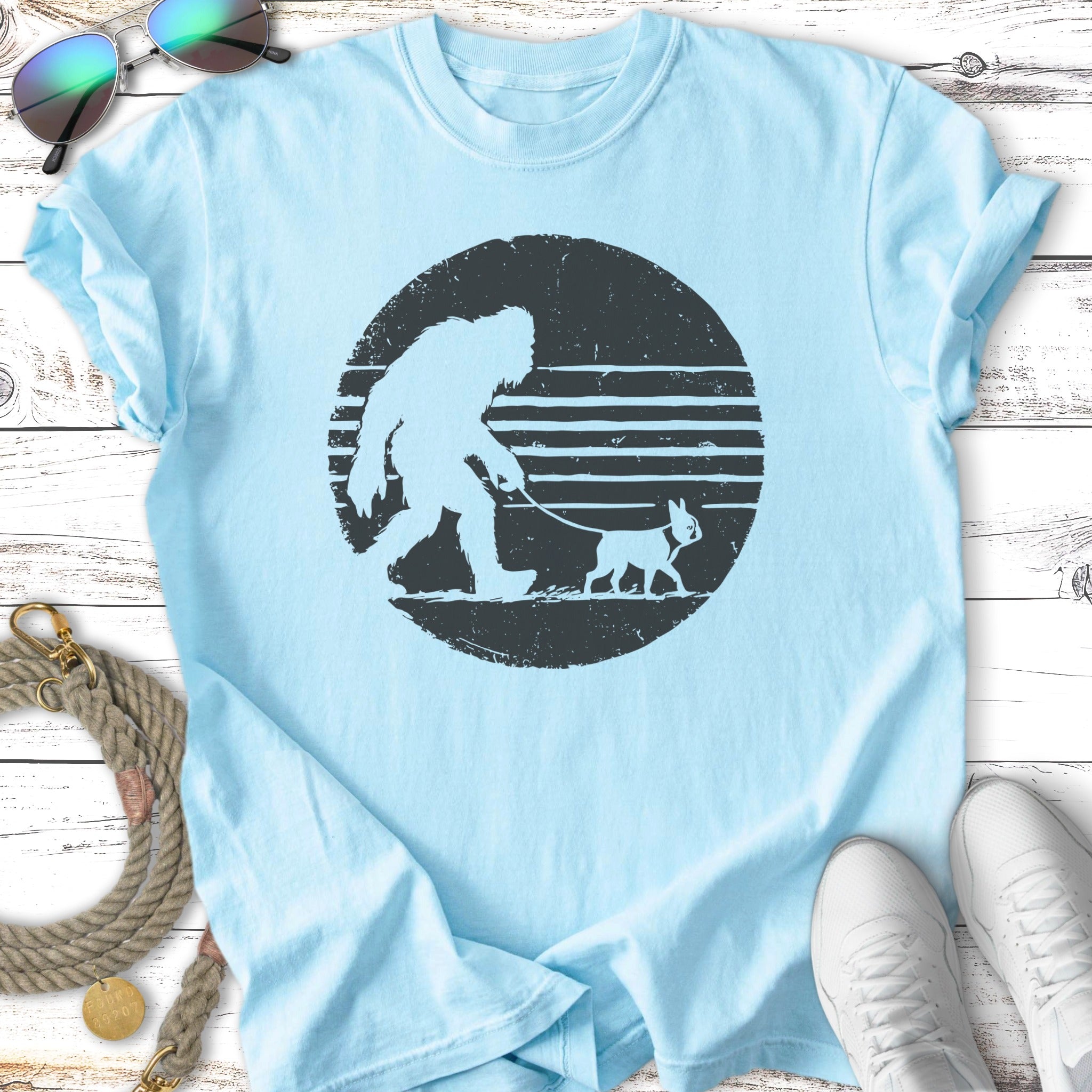 Light blue t-shirt with Bigfoot walking a small dog silhouette on a leash.