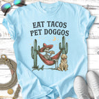 Skeleton in hammock with dog, eating tacos under a moon and cacti.