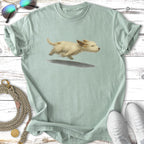 A small tan dog runs joyfully on a pale blue t-shirt.