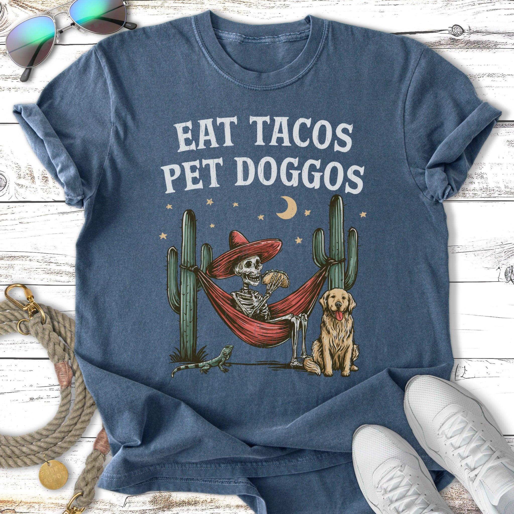 Skeleton in hammock eating tacos with dog and cactus.