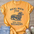 Orange t-shirt with grey text "REAL MEN Play With their WEINERS" and a dachshund illustration.