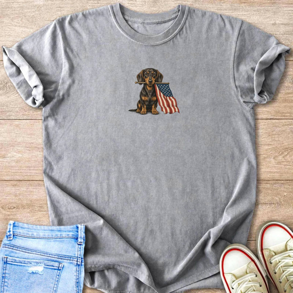 Dachshund holding American flag on grey t-shirt with jeans and sneakers.