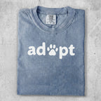 Blue t-shirt with white "adopt" text and paw print graphic.